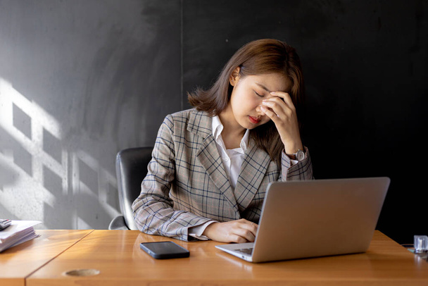Una mujer de negocios tiene un dolor de cabeza después de trabajar delante de su computadora portátil durante mucho tiempo y mirando un montón de papeleo que causa estrés, ella está descansando y trabajando duro. Concepto de síndrome de oficina. - Foto, Imagen