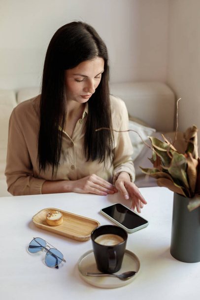 a woman uses a smartphone in a cafe. Freelancer. blogger - Zdjęcie, obraz