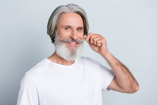 Portrait of attractive cheerful well-groomed gray-haired man touching moustache isolated over grey pastel color background. - Foto, afbeelding