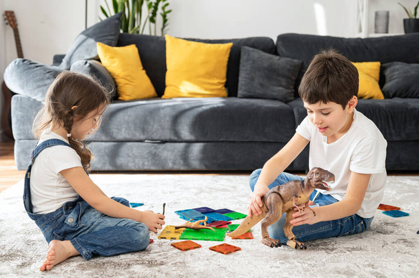 Children brother and sister playing with constructor on the floor in cozy living room while enjoying game together. Happy kids at home concept - 写真・画像