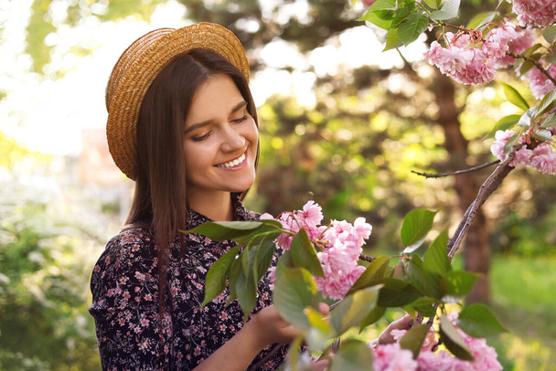 Beautiful young woman near blossoming sakura tree in park - Zdjęcie, obraz
