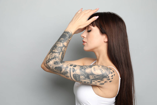 Beautiful woman with tattoos on arm against grey background - Photo, Image