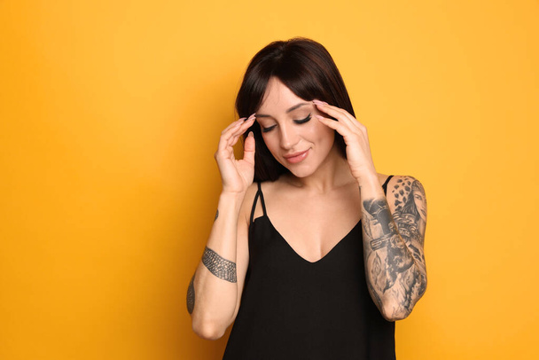 Beautiful woman with tattoos on arms against yellow background - Photo, Image