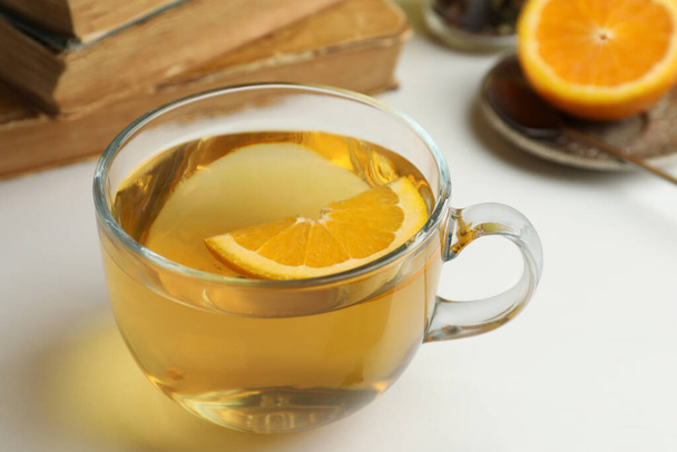 Glass cup of freshly brewed tea with orange on light table, closeup - Foto, afbeelding