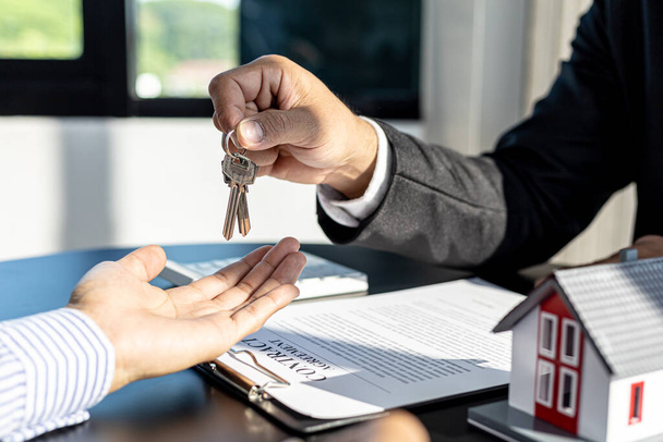 A home rental company employee is handing the house keys to a customer who has agreed to sign a rental contract, explaining the details and terms of the rental. Home and real estate rental ideas. - Photo, image