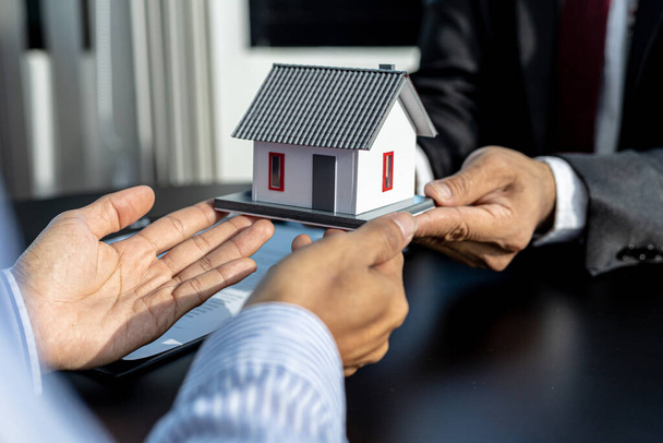 Two people holding a small model house, the home salesman handing over the house to the customer after signing the contract and inspecting the house. Real estate trading ideas. - Photo, Image