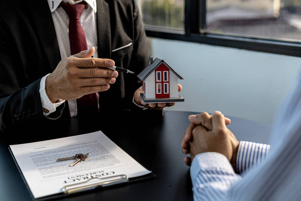 The property salesman on the project is pointing to a model of a small house to describe the structure and materials in the construction. Concept of selling housing estates and real estate. - Photo, Image