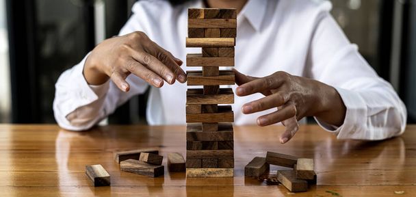 A woman is pulling a block of wood from a row and not breaking it down, like running a good business and solving problems. The concept of business management on risk. - Photo, Image