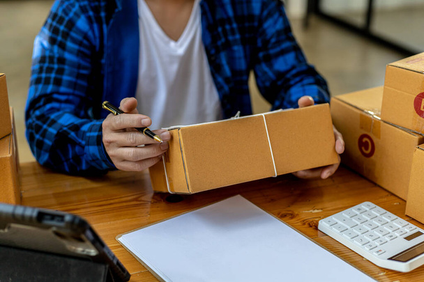 Asian person writing customer's shipping information on parcel box, He owns an online store, He ships products to customers through a private courier company. Online selling concept. - Foto, afbeelding