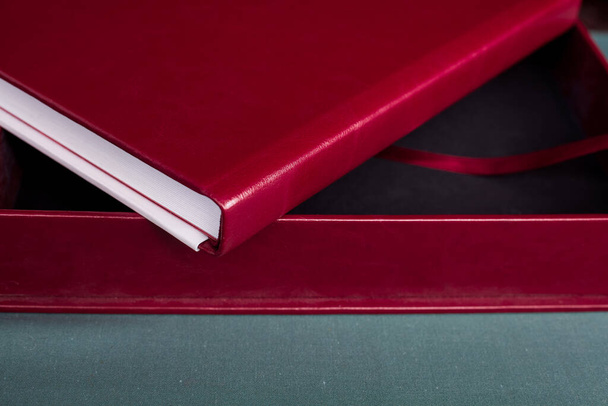 Uma grande caixa elegante e um caro prémio Borgonha photobook com uma capa de couro e páginas brancas encontram-se em uma mesa cinza dentro de casa. - Foto, Imagem