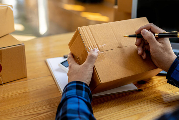 Asian man writing customer's shipping information on parcel box, He owns an online store, He ships products to customers through a private courier company. Online selling concept. - Fotó, kép