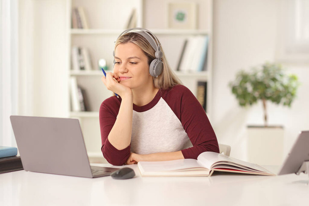 Γυναίκα φοιτητής που σπουδάζει μπροστά από έναν φορητό υπολογιστή στο σπίτι με ακουστικά  - Φωτογραφία, εικόνα