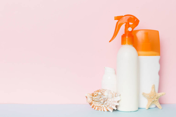 Beach accessories. Moisturiser sunscreen suntan lotion bottle for UVB skincare protection in summer with seashells on colored background. Mock up with copy space. - Фото, зображення