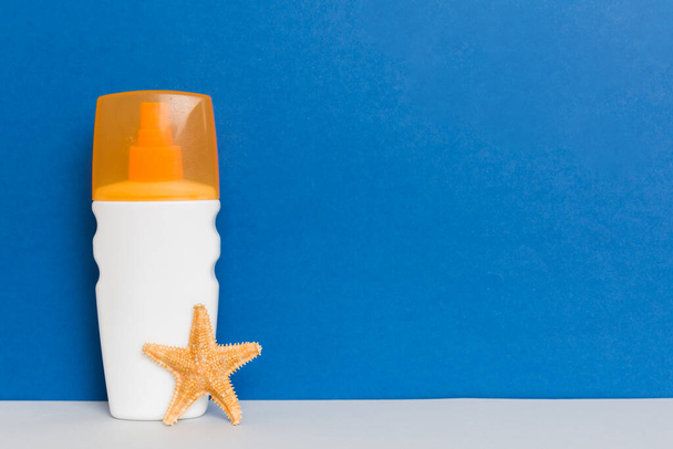 Beach accessories. Moisturiser sunscreen suntan lotion bottle for UVB skincare protection in summer with seashells on colored background. Mock up with copy space. - Φωτογραφία, εικόνα