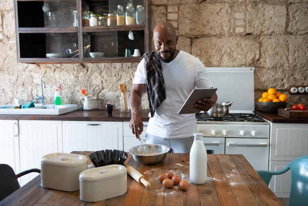 Afro american man cooking while looking at the recipe online on his tablet - Fotoğraf, Görsel