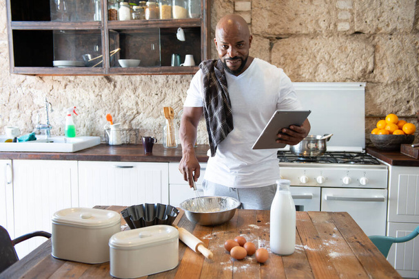Afro american man cooking while looking at the recipe online on his tablet - Photo, Image