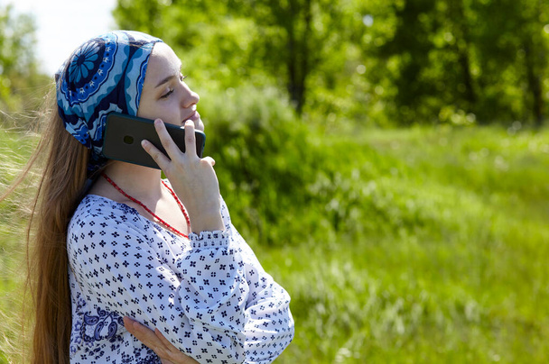 Attractive young woman talking with cellphone on the spring meadow. Close up portrait of happy hipster girl relaxing at nature and have a good time - Fotografie, Obrázek