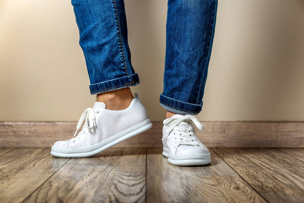 Uomo in Stylis New White Sneakers e jeans in piedi sul pavimento in parquet a casa - Foto, immagini