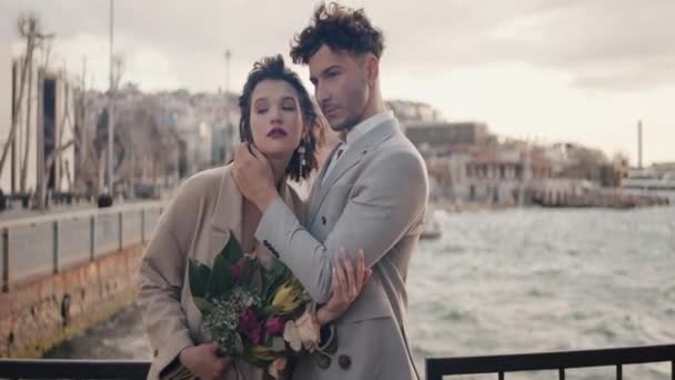 Beautiful wedding photo shoot with two models.Action.A young beautiful couple with a tall groom in suits and a bouquet of flowers are standing on the embankment and flirting with each other. High - Footage, Video