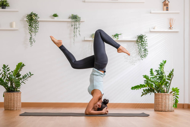 Side view of Asian woman wearing sportwear doing Yoga exercise in front of windows,Yoga Forearm Stand pose or Pincha Mayurasana.Calm healthy young female breathing and meditate yoga self care at home - Foto, imagen