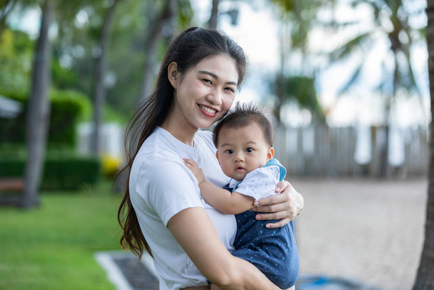 Happy Asian mom holding her newborn baby smile and spending time for good moment together. Adorable little baby boy having fun and cheerful with love from mother.Mother day concept - Фото, изображение