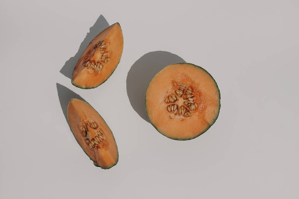Summer food still life composition. Halved and slice of cantaloupe melon fruit in sunlight. Harsh shadows overlay. Beige table background. Flat lay, top view, tropical design. - Photo, Image