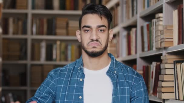 Lähikuva tyytymätön järkyttynyt intialainen mies opiskelija katselee kameraa seisoo kirjastossa osoittaa peukalo alas osoittaa paheksuntaa symboli alhainen pisteet epäonnistuminen tyytymätön koulutukseen - Materiaali, video
