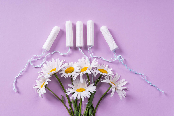 women's tampons and chamomile flowers bloom on a pastel lilac background. flat lay. idea women's health, menstruatio - Photo, image