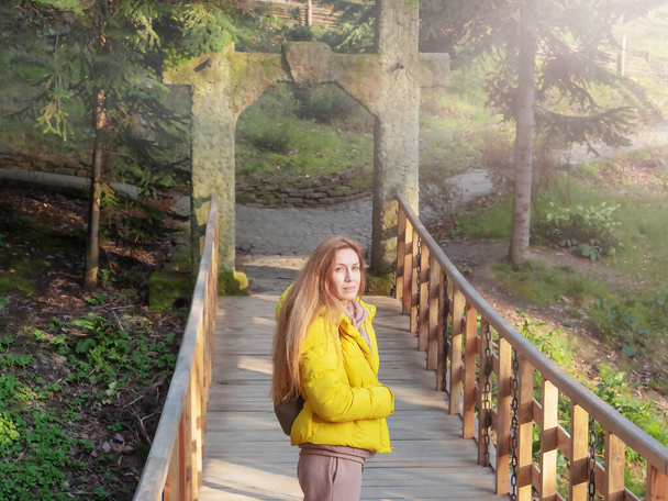 Turistka stojí na dřevěném mostě v jarním zeleném jehličnatém parku za slunečného dne. Měkké zaměření. - Fotografie, Obrázek