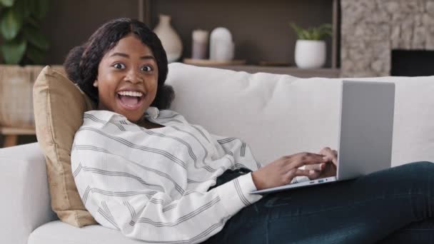 Afrikaans meisje student vrouw freelancer met laptop liggend op de bank het krijgen van goed nieuws bieden positieve hoge score voor test baan aankondiging geluk succes win schok verrassing verwondering wonder met computer app - Video