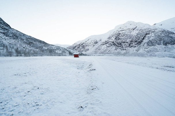 χιονισμένα βουνά της Νορβηγίας με ένα μικρό κόκκινο σπίτι στην απόσταση στην οποία οδηγεί ο δρόμος - Φωτογραφία, εικόνα