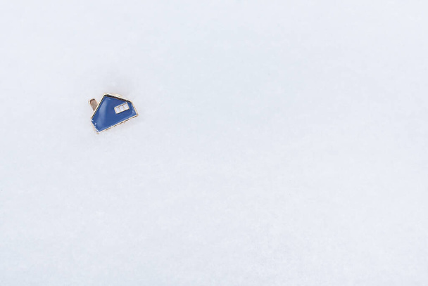 Una pequeña casa azul de metal que yace sobre la nieve. Lugar para una inscripción. Concepto inmobiliario e hipotecario - Foto, Imagen