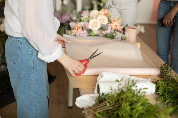 květinářská žena krájí papír na stole s rostlinami. Kvalitní fotografie - Fotografie, Obrázek