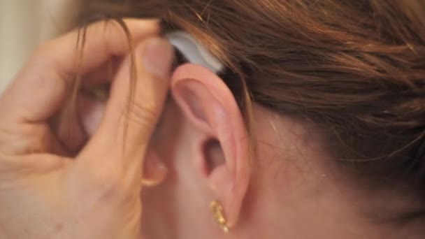 Nahaufnahme einer unkenntlichen Dame, die sich ein modernes Hörgerät auf ihr linkes Ohr legt - Filmmaterial, Video