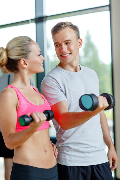 smiling young woman with personal trainer in gym - Фото, зображення