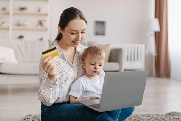 Happy young mother and her toddler son purchasing online with laptop and credit card, kid boy sitting on mom laps, shopping on web, buying toys or new clothes - 写真・画像