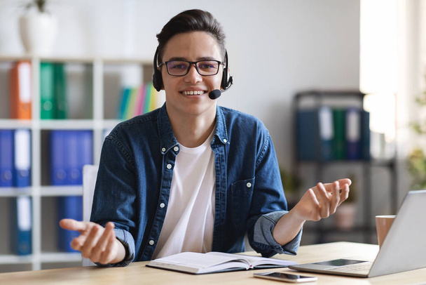 Telecommuting Concept. Portrait Of Handsome Call Center Operator At Workplace In Office, Happy Millennial Employee Wearing Headset, Consulting Client By Call And Smiling At Camera, Free Space - Photo, Image