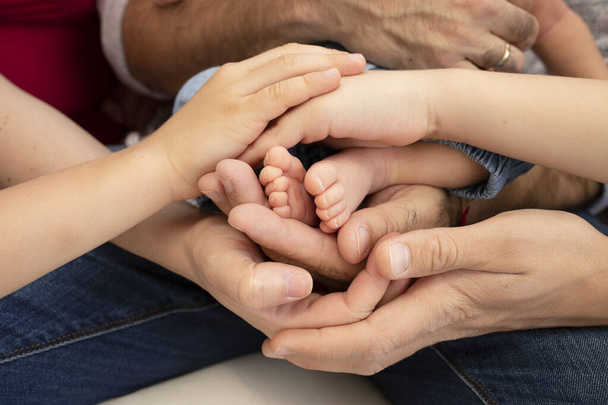 Many hands around the legs of a newborn baby, adults and children, a big family. Close up. Concept together, happiness, family values, parenthood, childhood, support. - Photo, image