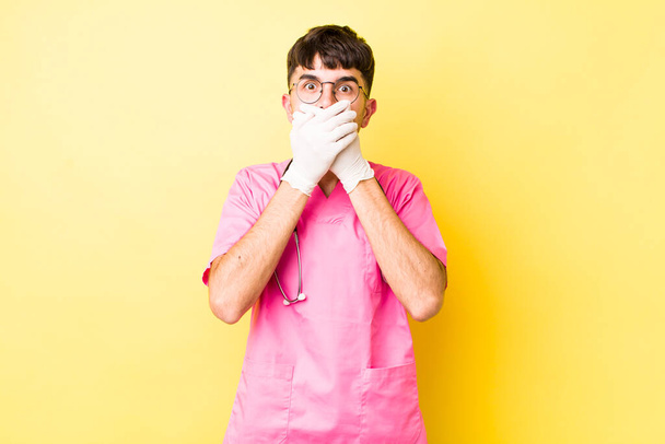 young hispanic man covering mouth with hands with a shocked. veterinarian concept - Zdjęcie, obraz
