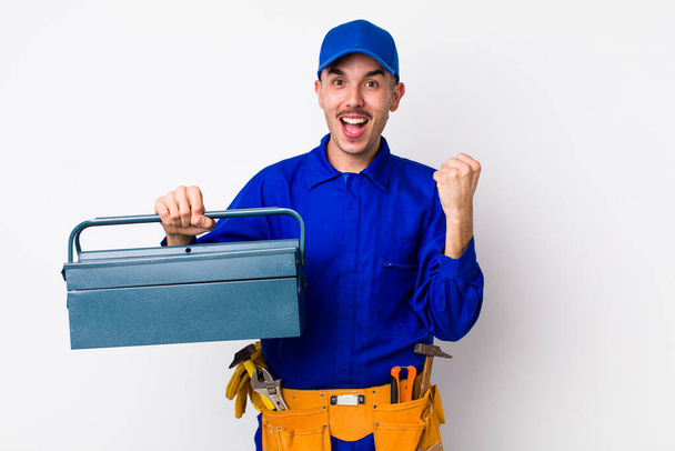 young hispanic plumber feeling shocked,laughing and celebrating success. toolbox concept - Photo, Image