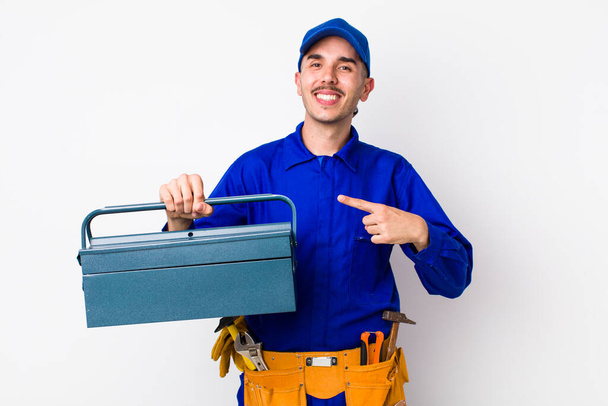young hispanic plumber looking excited and surprised pointing to the side. toolbox concept - Photo, image