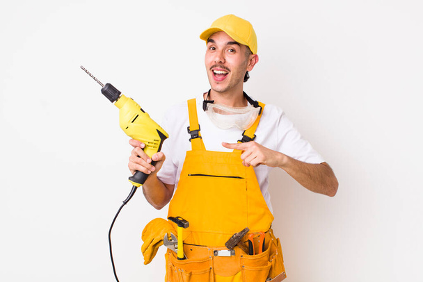 hispanic handyman looking excited and surprised pointing to the side. drill concept - Photo, Image