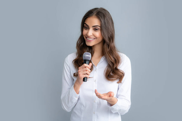 Красивая деловая женщина выступает на конференции. Счастливая улыбающаяся деловая женщина держит микрофон, стоит с микрофоном на сером фоне, в рубашке - Фото, изображение
