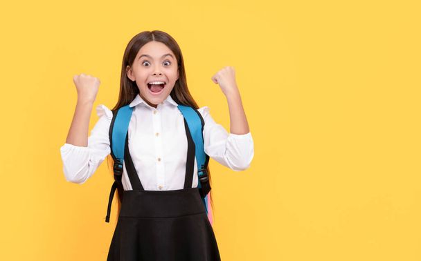 χαρούμενο παιδί με σχολική στολή κουβαλάει σακίδιο γιορτάζει την επιτυχία, την ευτυχία. - Φωτογραφία, εικόνα