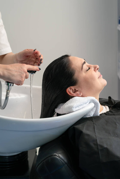 le cosmétologue lave la tête de la fille avec un shampooing pour d'autres procédures. cheveux noirs. plus la taille. - Photo, image