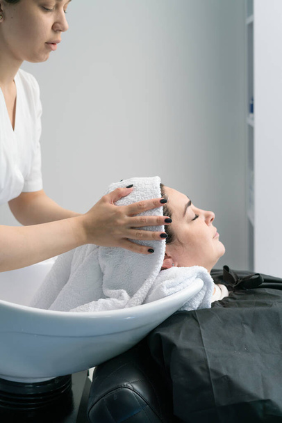 Косметолог сушит голову полотенцем клиенту. раковина, черные волосы, плюс размер - Фото, изображение