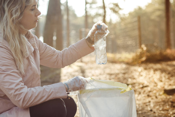 Droevige vrouw vrijwilliger en assistent schoon natuurlijk bos van plastic afval, afval. Plastic flessen verzamelen om in te pakken. Ecologisch recyclingprobleem, vervuiling, opwarming van de aarde. Duurzame ontwikkeling - Foto, afbeelding