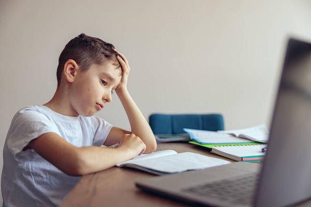 Retrato de un niño triste cansado y perezoso que tiene una lección de video en línea en la computadora portátil. Educación en el hogar. - Foto, imagen