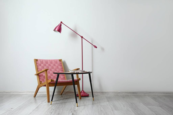 Poltrona confortável, mesa e lâmpada de assoalho perto da parede clara na sala   - Foto, Imagem