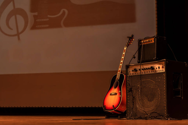 акустическая гитара на гитарной стойке с двумя усилителями рядом с ней im spain - Фото, изображение